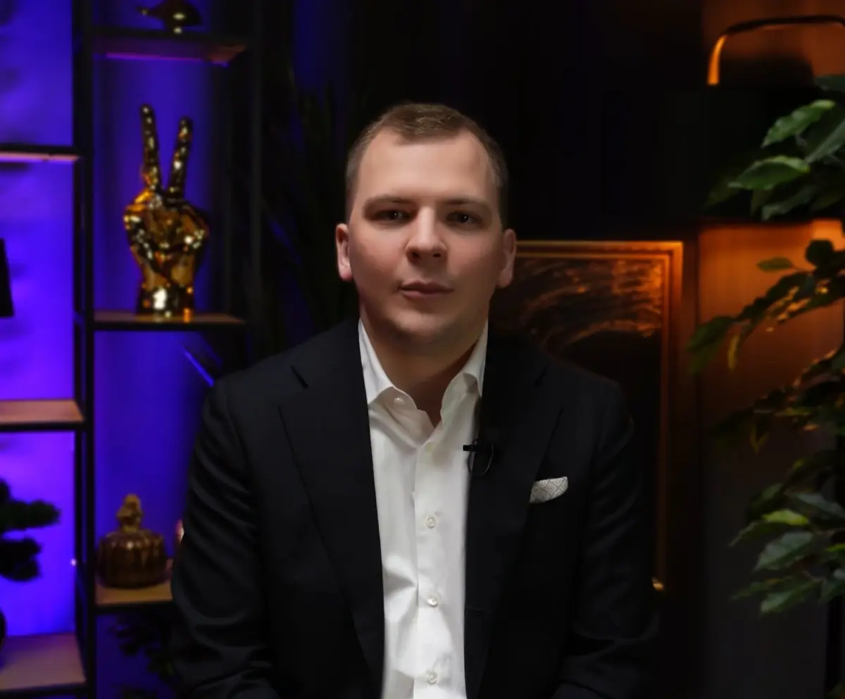 Гость в тёмном пиджаке на площадке, за ним на полке золотая фигура руки